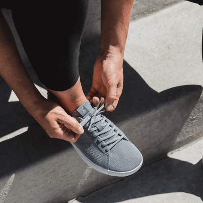 Woman Tying Grey and white athleisure barefoot casual crossfit workout shoes #color_concrete-grey-recycled