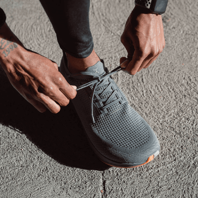 Lifestyle image of man tying grey running shoes #color_grey-gum-rn